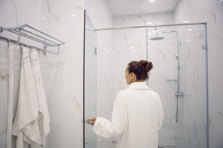 woman standing in the bathroom next to the shower cabin in hotel apartment in a white robe